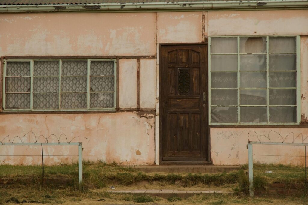 Front view of an abandoned house with a rustic wooden door and cracked walls, reflecting decay.