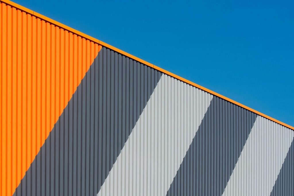 Abstract view of a modern industrial facade with orange and gray stripes under a clear blue sky.