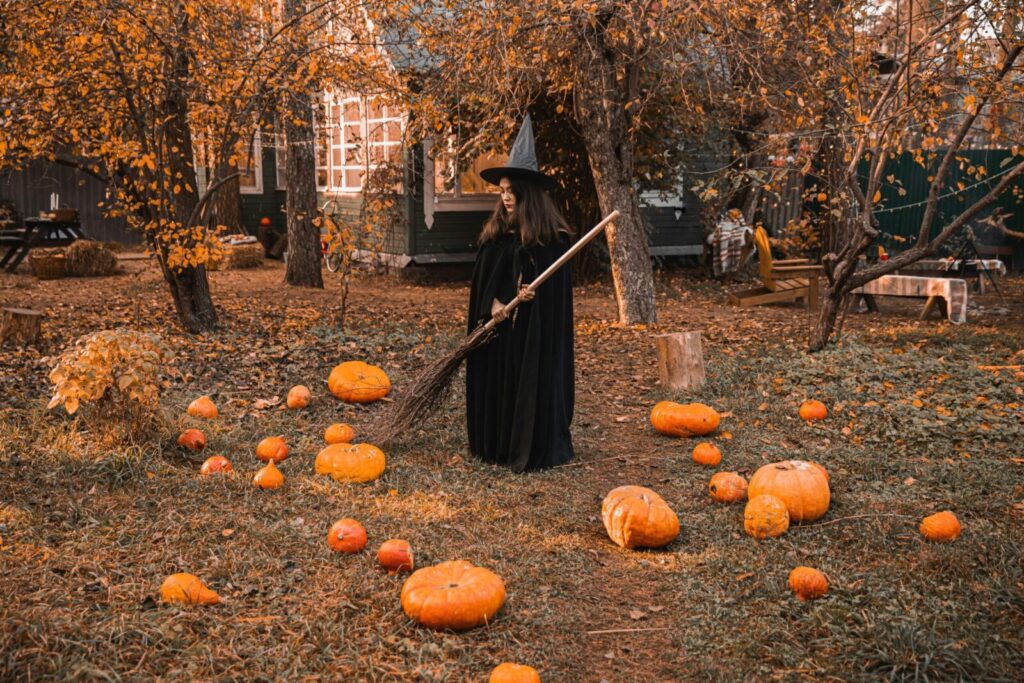 A witch in a classic costume stands among pumpkins in a fall-themed backyard, creating a perfect Halloween vibe.