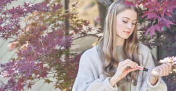 Young woman applying essential oil to wrist surrounded by autumn leaves.