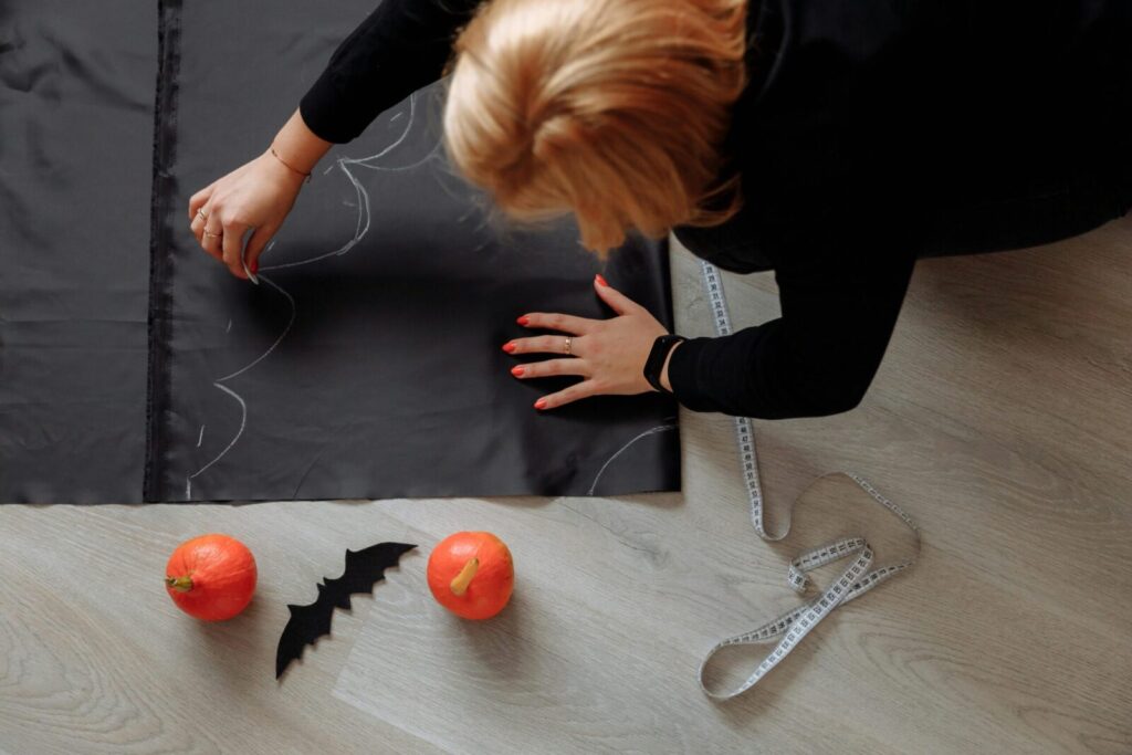 A woman crafting a Halloween costume indoors with pumpkins and fabric.