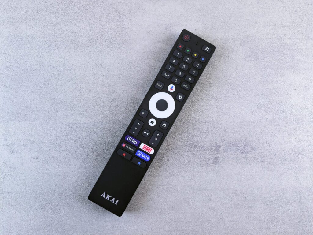 Close-up of a black remote control with buttons, placed on a grey textured surface.