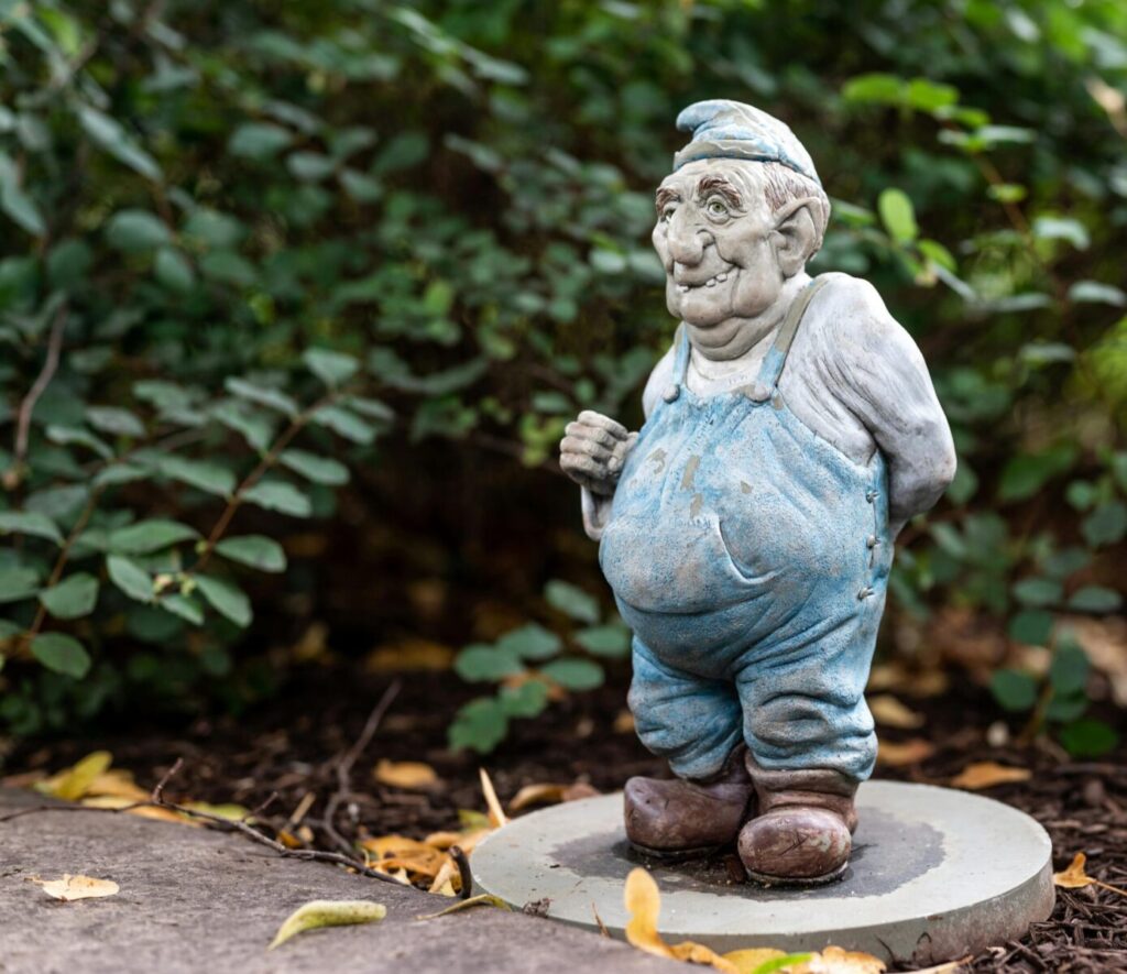 Whimsical garden gnome sculpture with a smiling face among green foliage, captured in a close-up outdoors.
