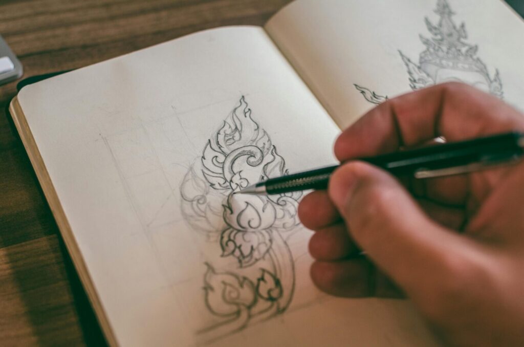 Close-up of a hand sketching detailed design in a sketchbook with mechanical pencil.