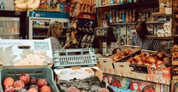 woman in brown long sleeve shirt standing in front of fruit stand
