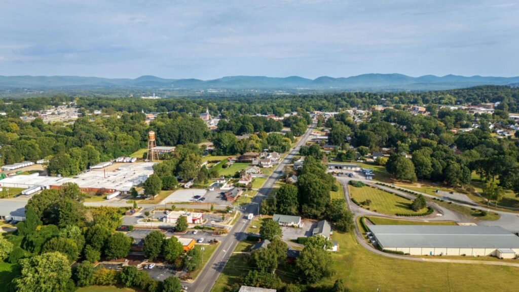 Aerial scenery of a town with lush greenery and distant mountains under clear skies.