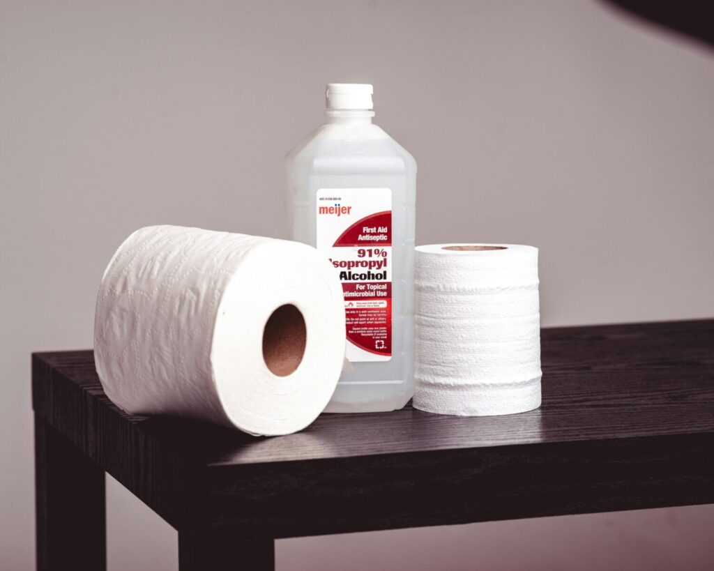 Close-up of isopropyl alcohol bottle and tissue rolls on a wooden table, emphasizing hygiene.