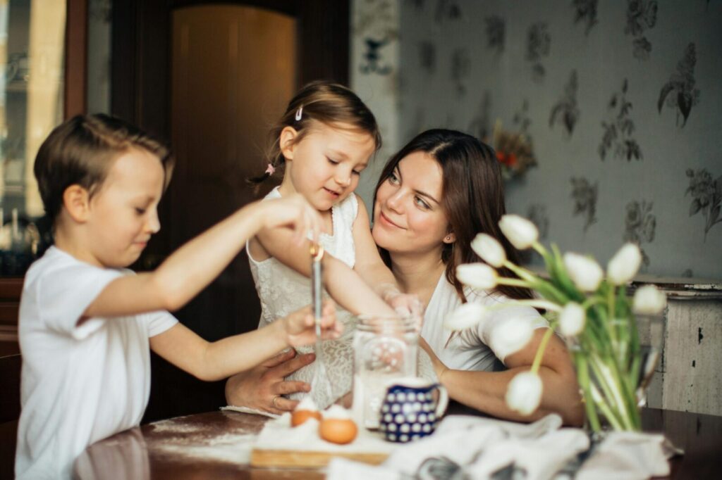 A loving mother and her two children baking and sharing joyful moments at the kitchen table.