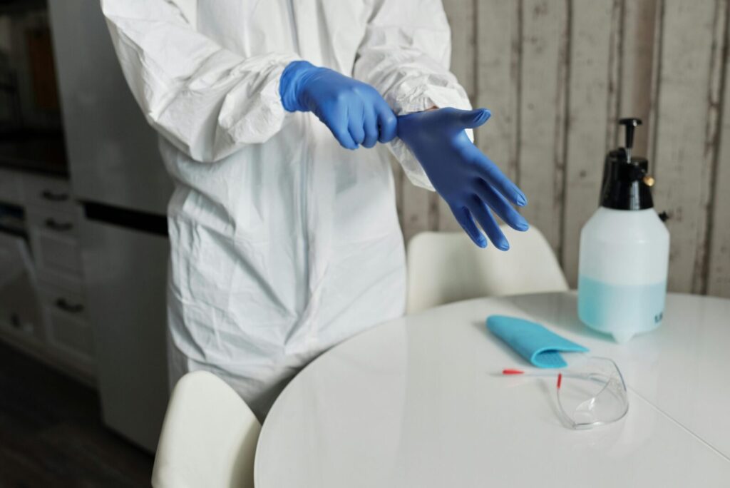 Individual wearing protective gear, preparing for cleaning with gloves and sanitizer.
