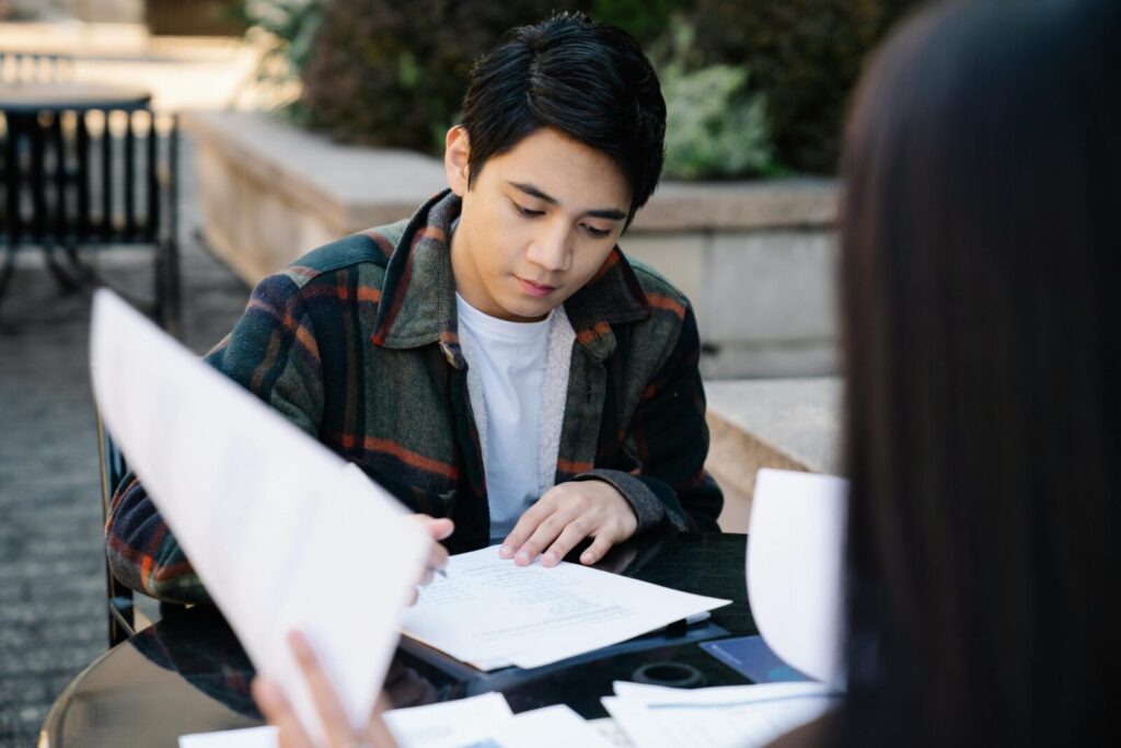 A focused young Asian man studying at an outdoor table, preparing for exams.