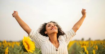 Joyful woman with arms raised in a sunflower field, embracing freedom and happiness.
