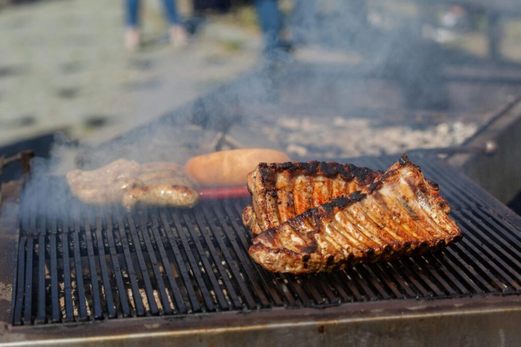 Grilling smoky ribs and sausages on an outdoor barbecue with visible smoke.