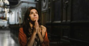 A woman is praying with hands clasped in a dimly lit church, creating a contemplative mood.