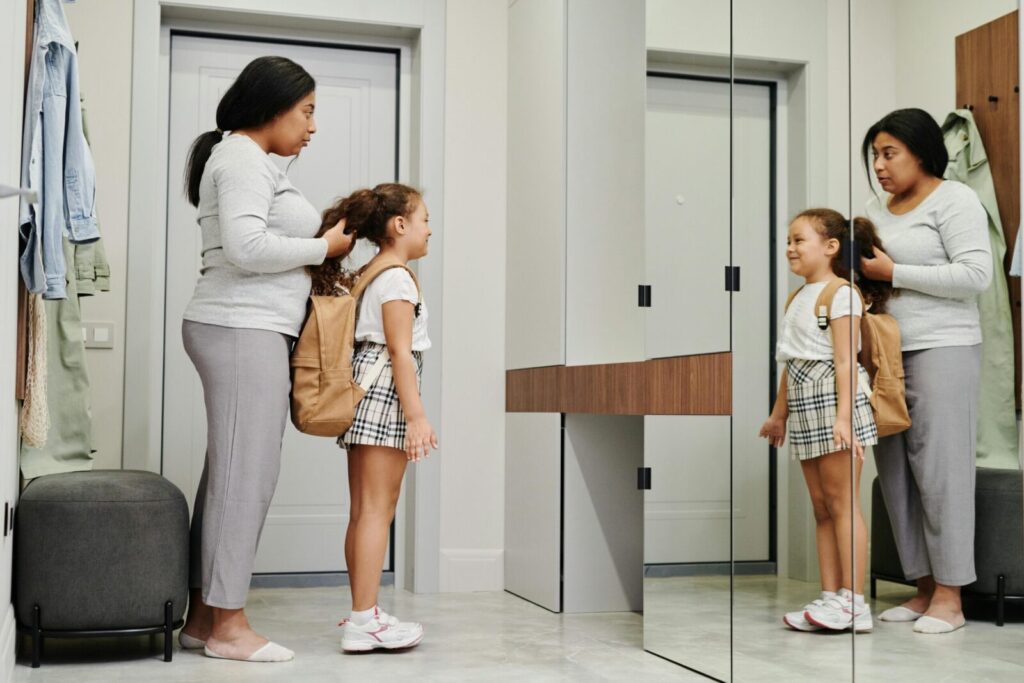 A mother and daughter preparing for school in front of a mirror, showcasing morning routines.