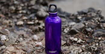 Close-up of a purple water bottle on rocky ground, perfect for outdoor adventures.