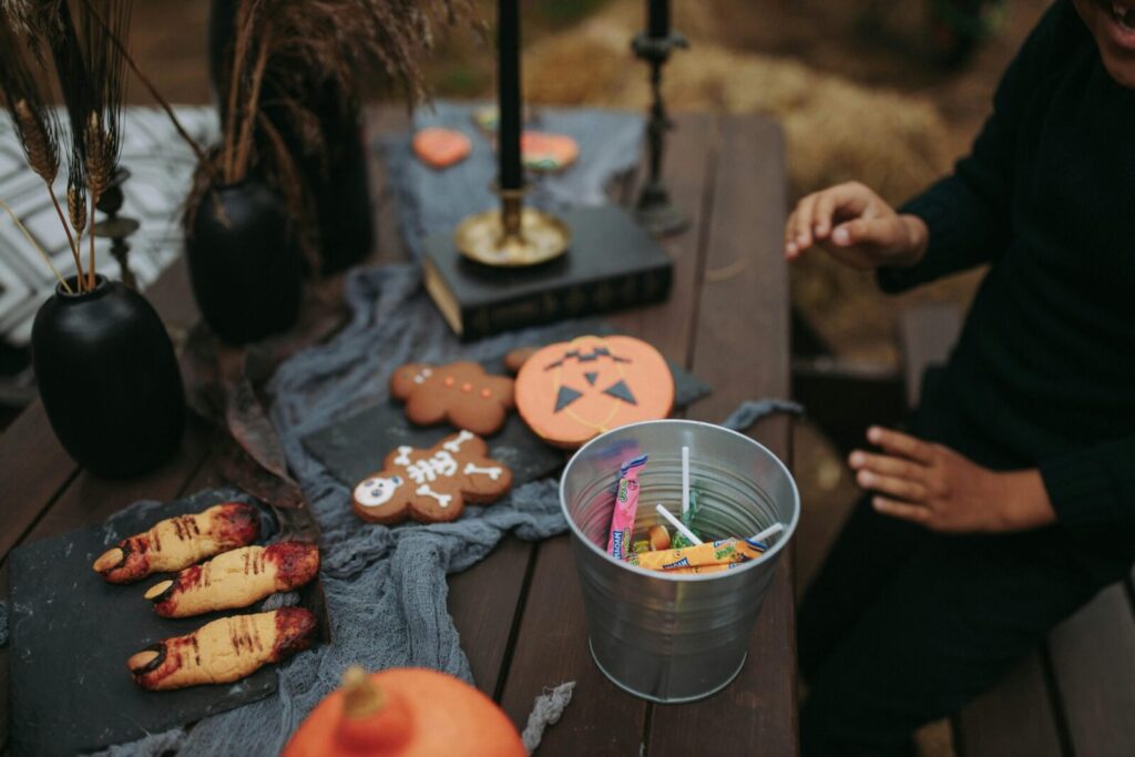 A festive Halloween setup with sweets, cookies, and spooky decorations on a wooden table.
