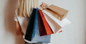 Woman holding colorful shopping bags against a wall.