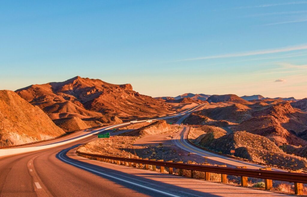 Stunning view of a winding highway amidst Nevada's rugged landscape under blue skies at sunset.