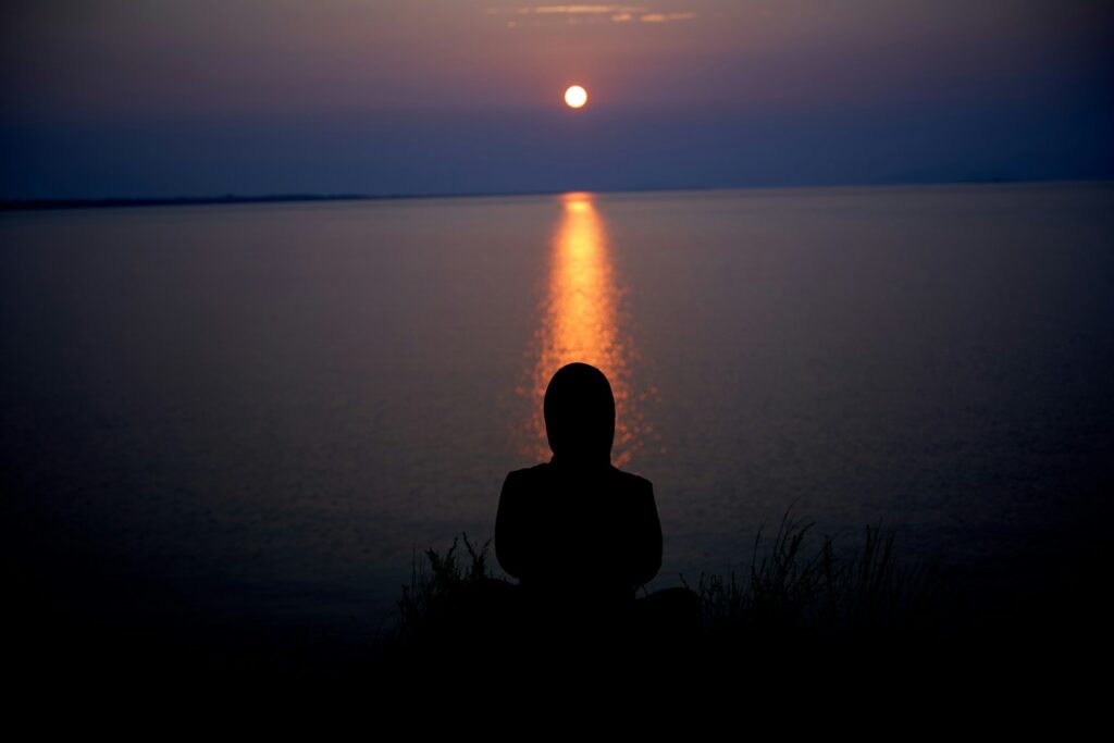 silhouette of person sitting on grass during sunset