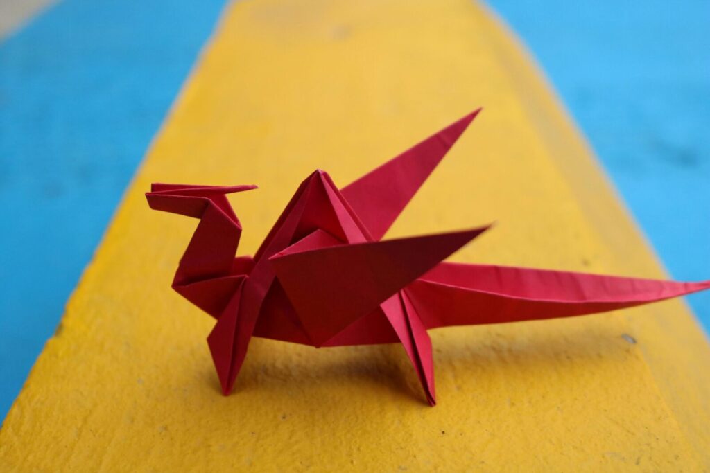 Vibrant red origami dragon displayed on a striking yellow and blue background.