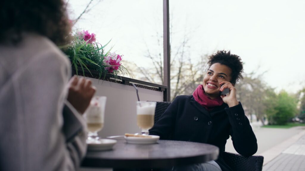 Two women talking and drinking at an outdoor cafe.
