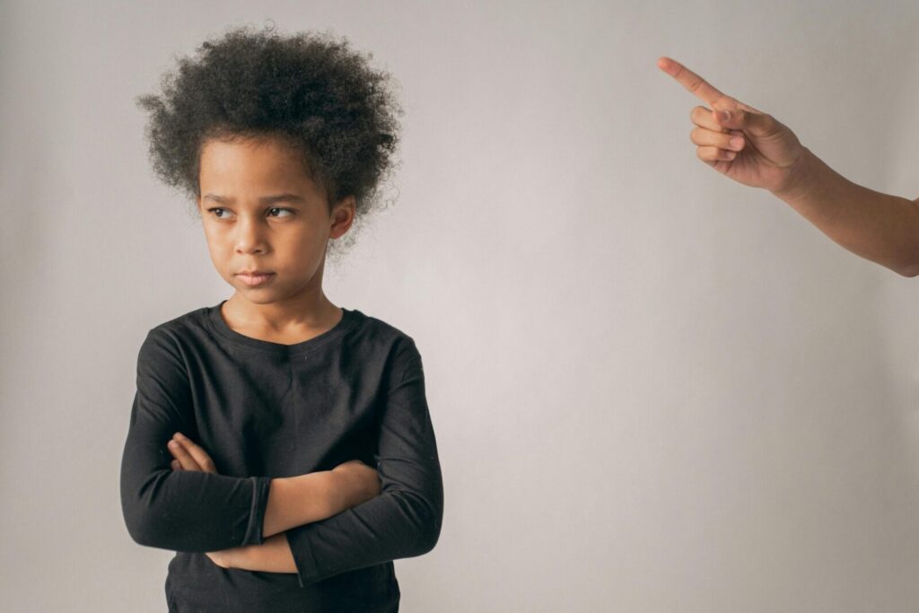 Young girl with arms crossed looks displeased as finger points, conveying discipline.