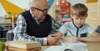 Grandfather helps grandson with homework at desk.