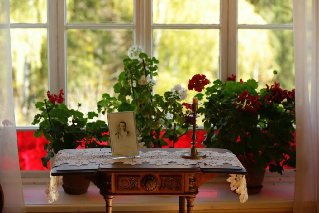 A vintage wooden table with flowers and a candle by a sunny window, evokes nostalgia.