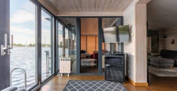 Contemporary design of spacious room made from natural materials and colors with overlooking rippled lake surface right behind floor to ceiling windows