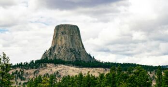 a large rock formation in the middle of a forest with Devils Tower in the background