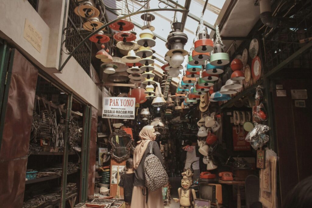 Woman shopping in a vibrant indoor market filled with various items and hanging lamps.
