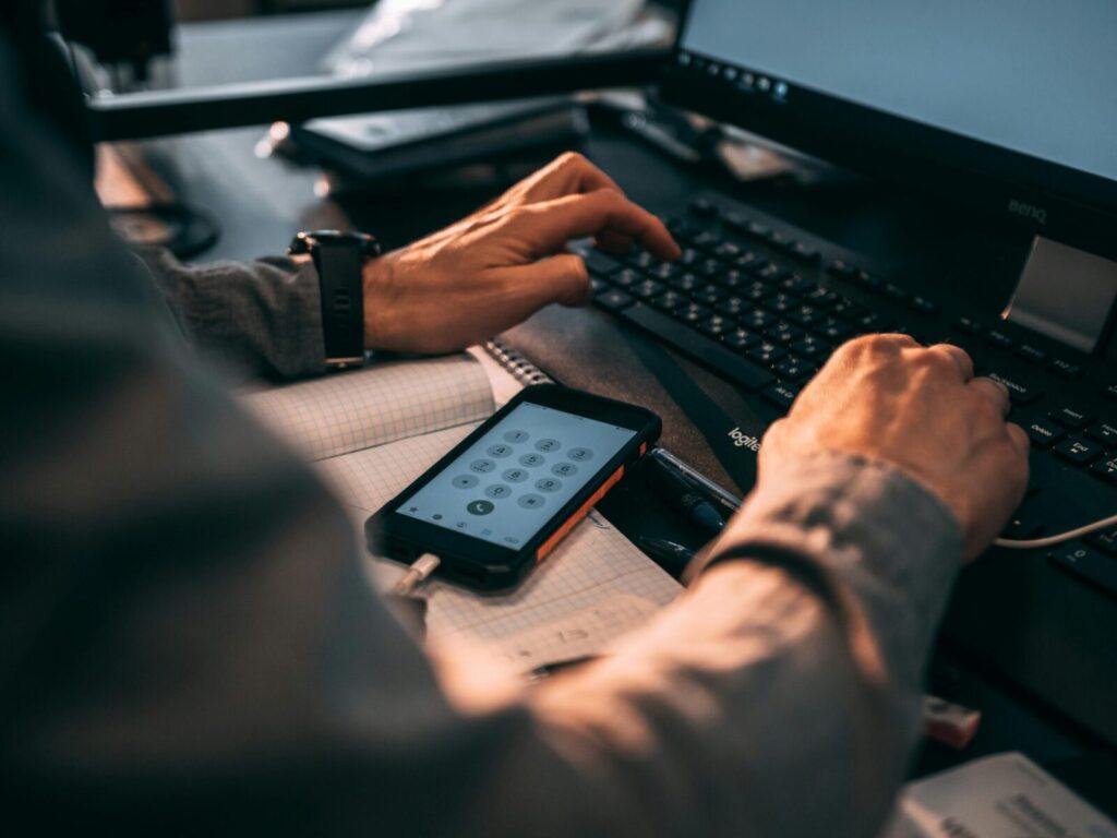 Businessman typing on keyboard in office with smartphone displaying numbers.