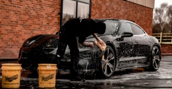 man in black jacket and pants leaning on black car