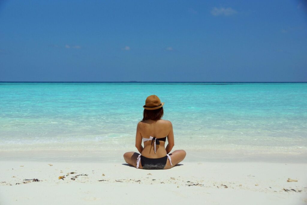 Rear view of a woman in a bikini and hat relaxing on a pristine beach in Maldives.