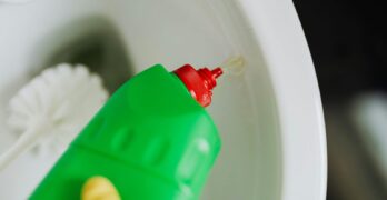 A person wearing a glove pours cleaning liquid into a toilet for sanitation.
