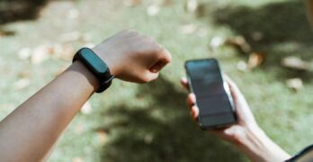 An individual checking both a smartwatch and smartphone outdoors with a blurred grass background.