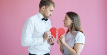 Couple holding broken heart halves on pink background