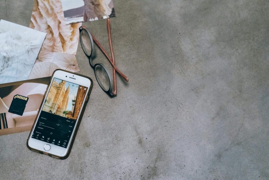 Mobile phone and eyeglasses on a concrete surface with photographs and a memory card.