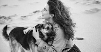A woman lovingly embraces her dog on a serene beach, capturing a moment of pure joy.