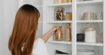 Woman arranging jars on pantry shelves for organized food storage.