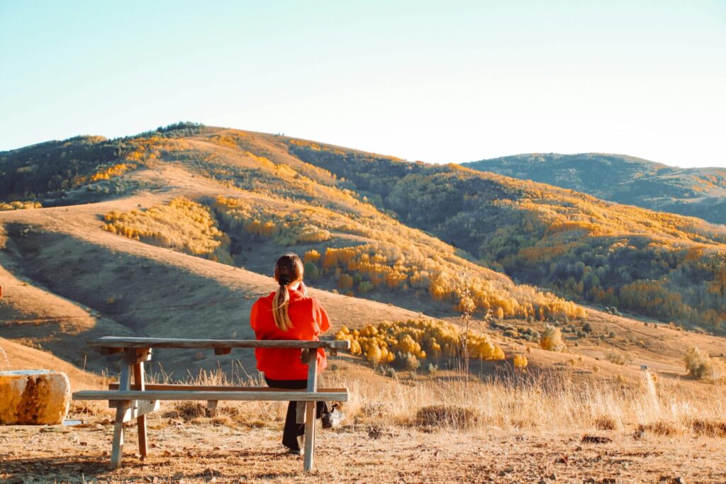 A woman sitting on a bench, admiring a stunning autumn mountain landscape.