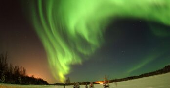 Vibrant green aurora borealis lighting up the snowy winter night sky in a remote wilderness.