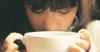 Woman savoring the aroma of a hot coffee cup in a cozy setting.