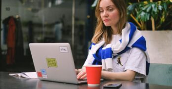 Young woman focused on laptop work in a modern cafe setting, surrounded by technology.