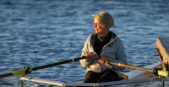 A woman rows her boat on calm water.