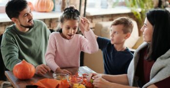 A joyful family crafting Halloween decorations together with pumpkins indoors.