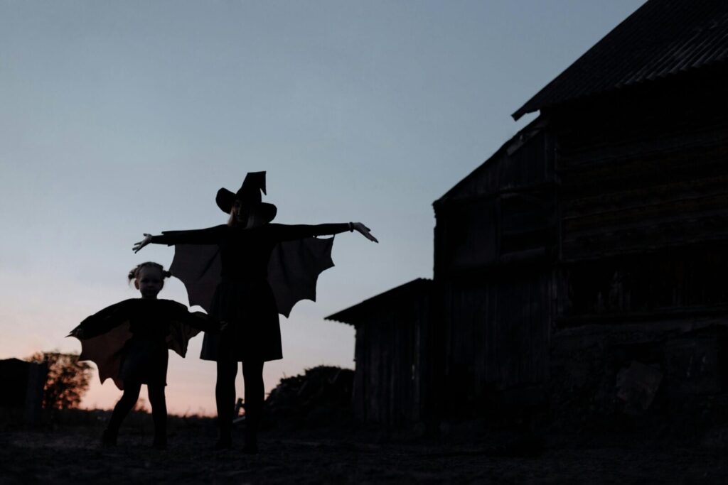 A whimsical silhouette of a witch and child playing in costumes at sunset. Perfect for Halloween and fantasy themes.