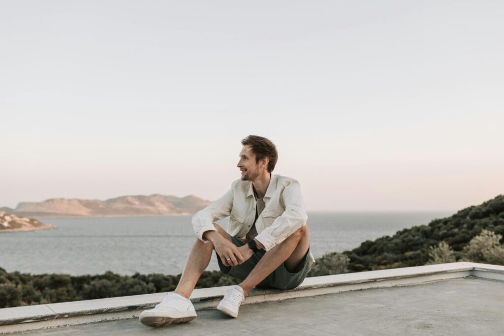 A man sits smiling with a scenic ocean view in Antalya, Turkey at sunset.
