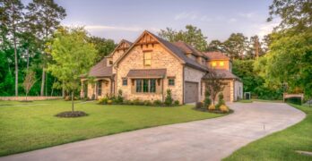 Elegant stone family home surrounded by trees, lush lawn, and vibrant garden.