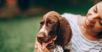 Smiling woman with a German Shorthaired Pointer enjoying a happy outdoor moment.